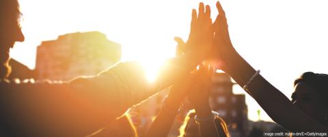 silhouetted group of people high-fiving at sunset with sunglare effect