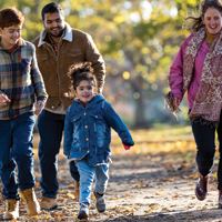 photo of hispanic dad and white mom walking outside through a park in the fall season with their daughter and son