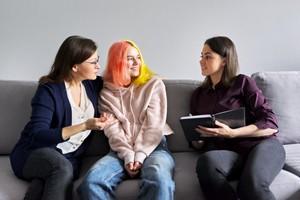 Teen girl with dyed hair with woman on couch talking with counselor